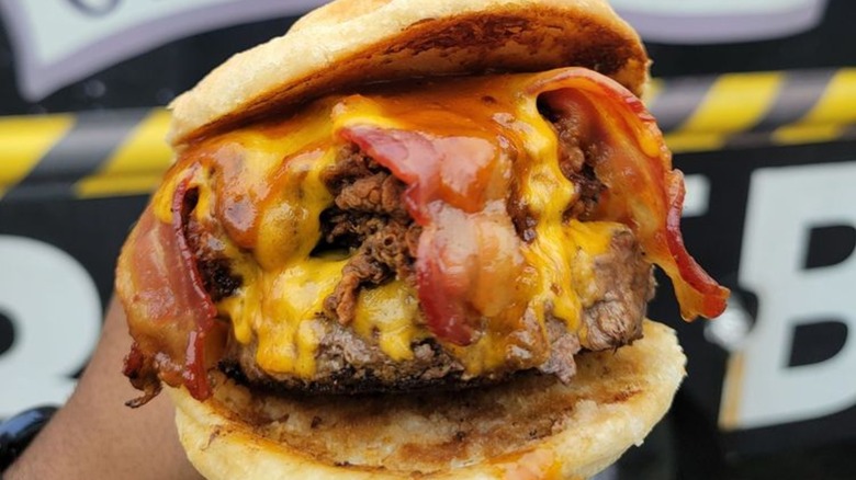 Hand holding cheeseburger wtih bacon and fried chicken