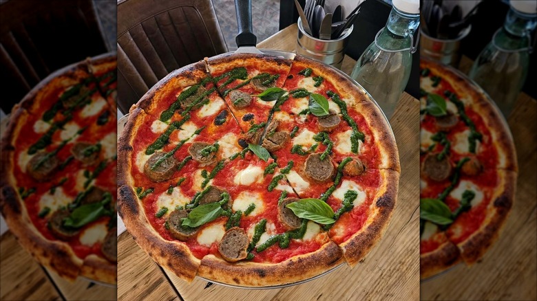 Pizza topped with mozzarella, pesto, sausage, and basil