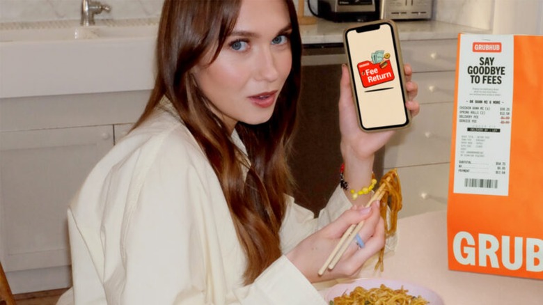 Veronika Slowikowska holding up a smartphone with the Grubhub Fee Return logo