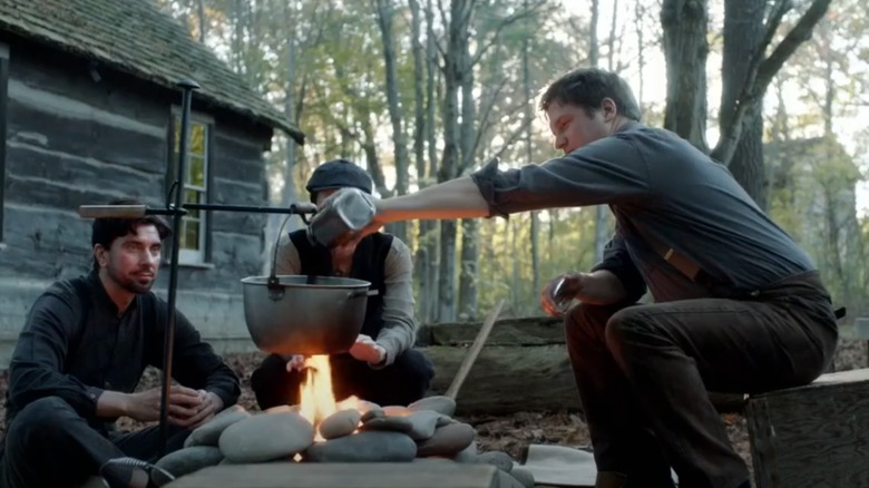 Three people sitting around campfire making coffee