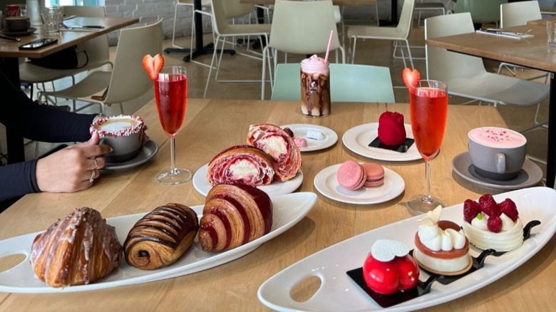 Table in restaurant set with plates and an assortment of pastries, croissants, macarons, and drinks