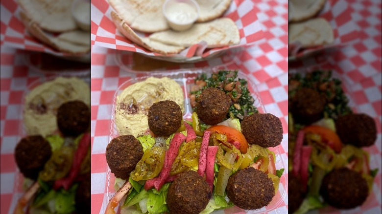 Taboulleh, hummus, falafel, and salad in a plastic takeout container on a checkered tablecloth