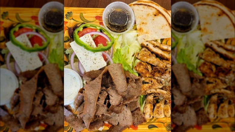Souvlaki, gyro meat, salad, pita, and feta on a decorative yellow plate