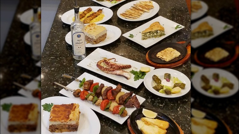 A spread of Greek dishes like octopus, spanakopita, and moussaka on a marble counter