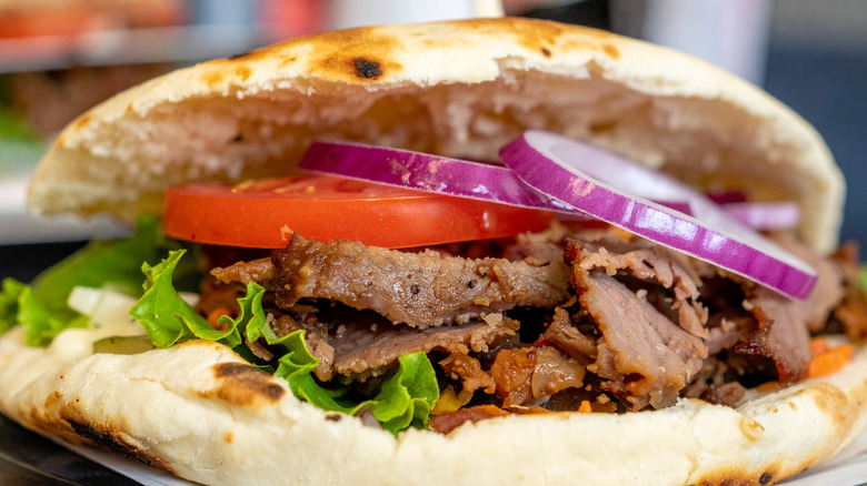 A close-up of a gyro with thinly sliced meat in a fluffy pita