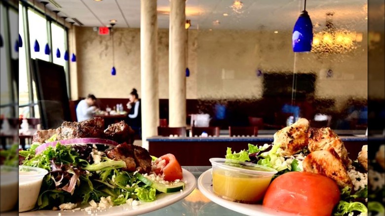 Two salads on a restaurant counter with a spacious dining room in the background