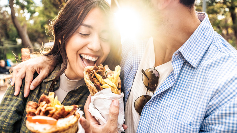 A couple holding gyros outside on a sunny day