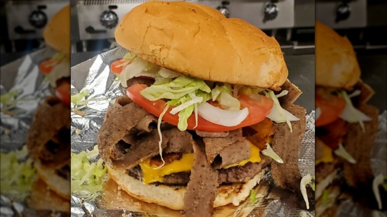 A burger with cheese, lettuce, tomato, onion, and gyro meat on foil