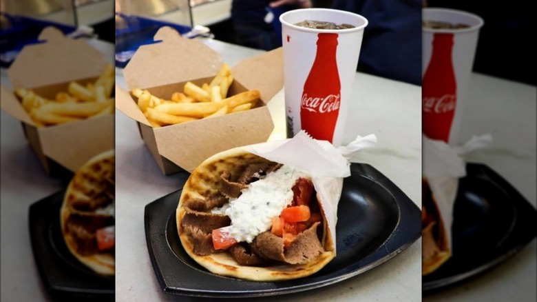 A gyro with tomato and tzatziki, a soda, and a paper container of french fries