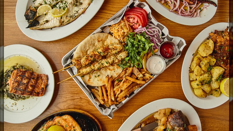 A spread of Greek dishes with souvlaki, pita, toppings, and fries in the center