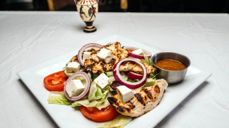 Grilled chicken over a salad with feta on a white tablecloth