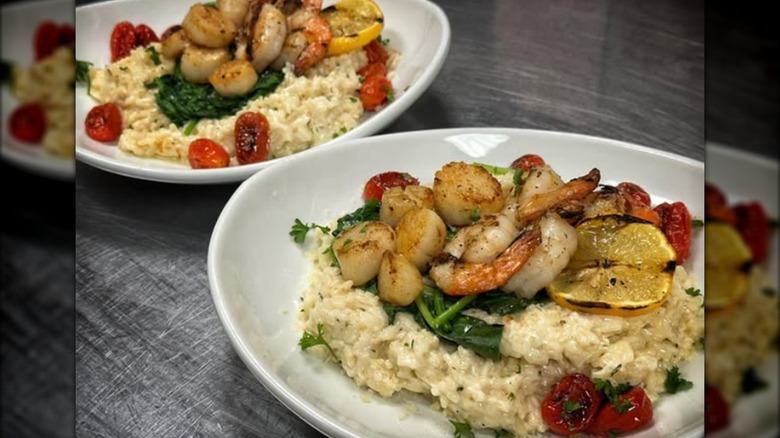 Two dishes of shrimp, scallops, tomatoes, and spinach over rice
