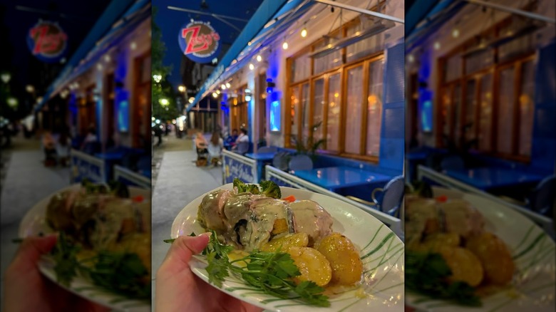 A hand holding a dish in front of the outside of Zesty's at night