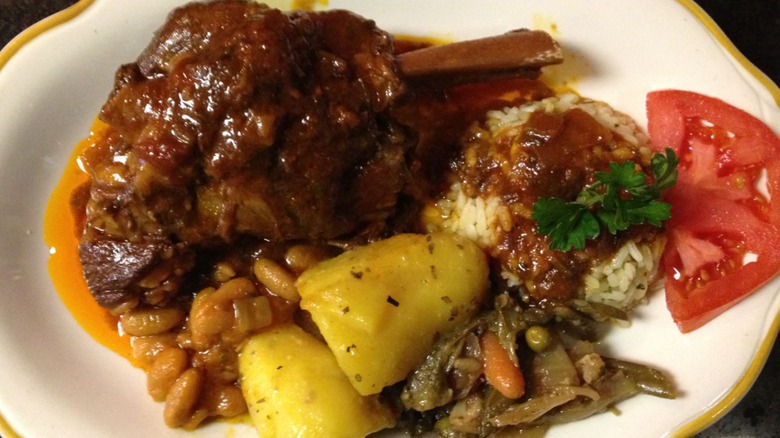 A close-up of a lamb shank dish with lemon potatoes and rice