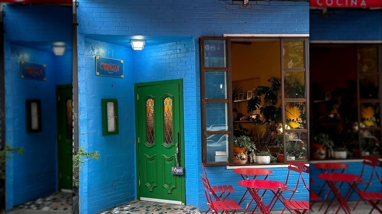 Exterior of Cocina Conseulo with blue tiles, green doors, and red chairs and tables