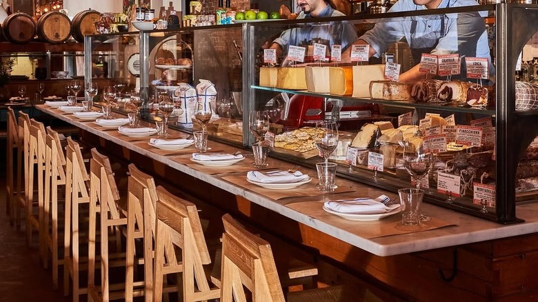 Counter seating at Il Buco Alimentari in NYC with a display case filled with cheese and Italian cold cuts