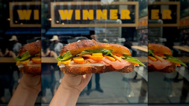 A person holding a sandwich in NYC with Winner sign in the background