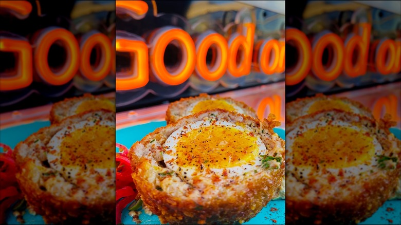 Scotch egg sliced in half in front of neon sign