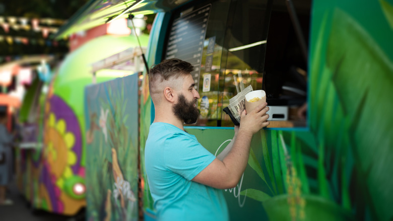 Smiling guy collecting his order from the window of a green food truck