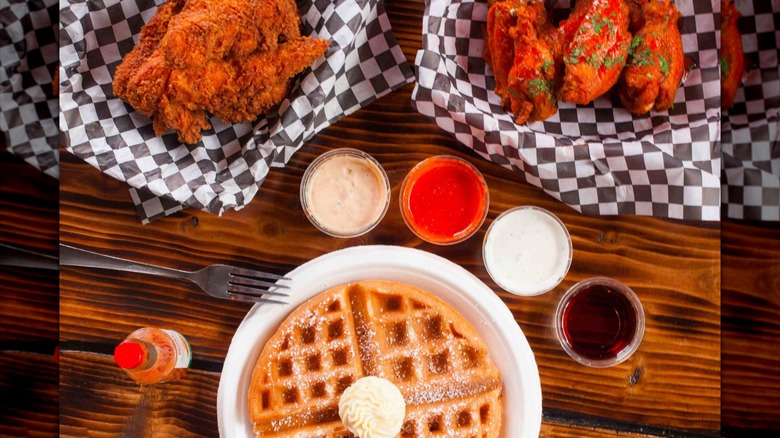 Waffles, fried chicken, and chicken wings with dipping sauce on wooden table