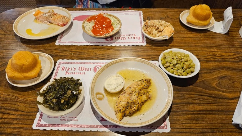 Assortment of dishes on table including fish, beans, collard greens, and rolls