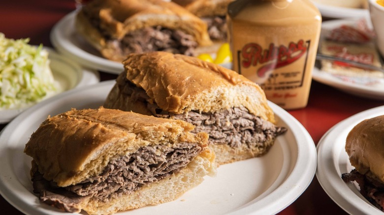 Two halves of a French dip on on plate with other sandwiches blurred in background