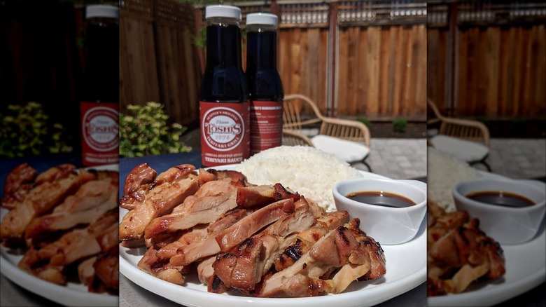 Plate of teriyaki with rice and sauce and bottles of sauce in background