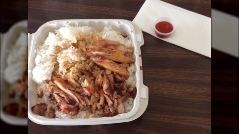 Teriyaki and rice in a takeout container on wood-grain table