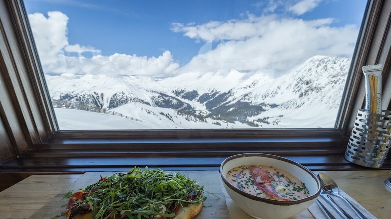 View of snowy mountains from a window at il Rifugio with lobster bisque and flatbread in the foreground