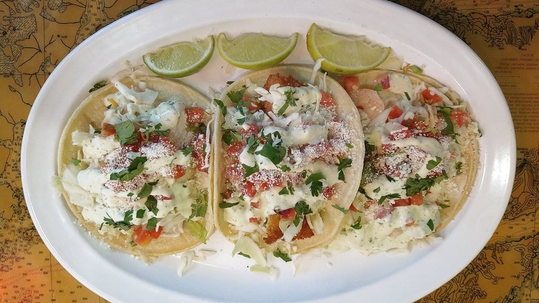 Three fish tacos on plate with slices of lime
