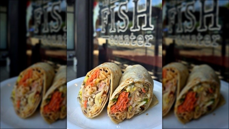 Halved wrap with salmon and slaw on plate with blurred sign in background