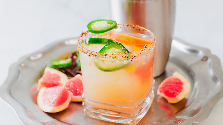Grapefruit mezcal margarita cocktail in glass, garnished with grapefruit wedges and jalapeño slices