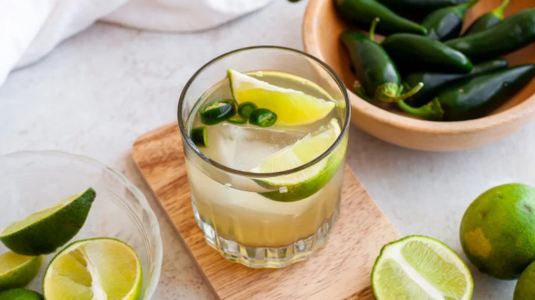 Spicy margarita cocktail in glass with sliced jalapeños and lime wedges