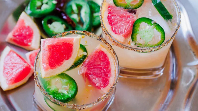 Mezcal margaritas in two glasses with grapefruit wedges and jalapeño slices