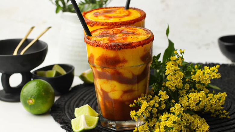 Two spicy mangonada cocktails in glasses, next to bunch of yellow flowers