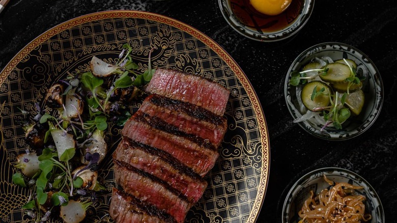 Sliced steak with green on a plate with side dishes