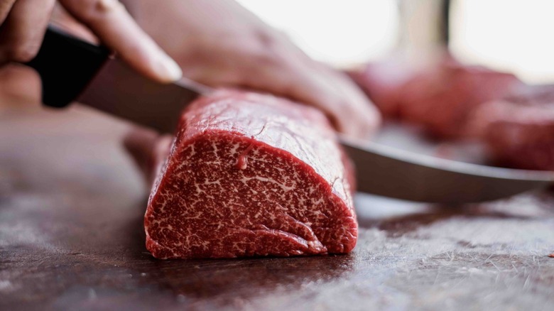 Hands and a knife, cutting slices of raw steak