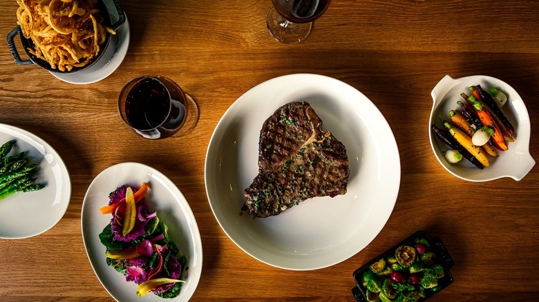 Aerial photo steak and assorted side dishes on white plates with wine