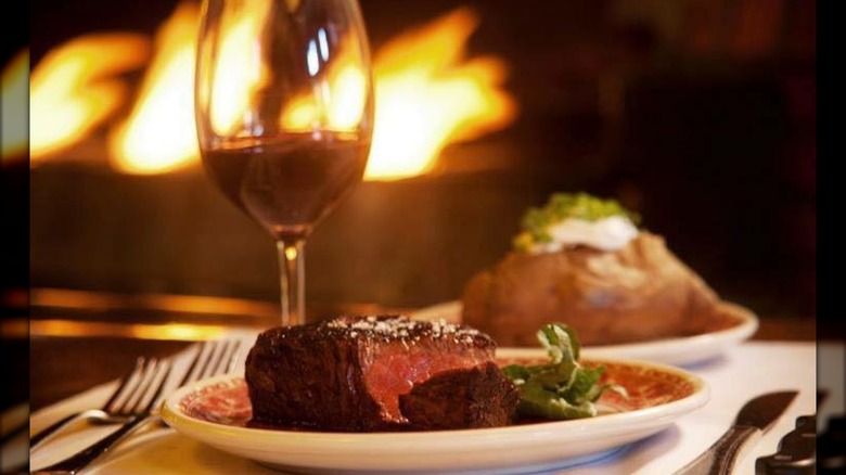 Steak on a plate with a glass of wine, baked potato, and fire background