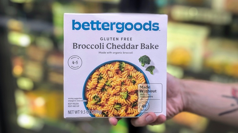 A hand holds a box of frozen broccoli cheddar pasta bake in the freezer section of Walmart