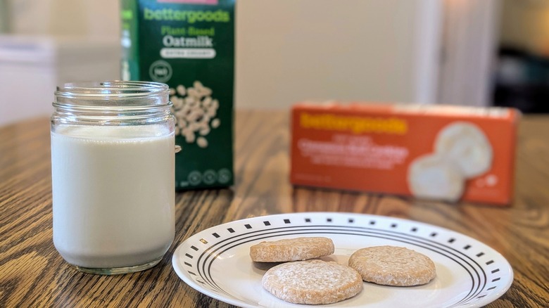 A plate of cookies and a glass of milk with a milk carton and cookie box behind it on a wood table