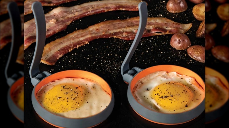 Blackstone Egg Rings, with eggs inside, on a Blackstone griddle along with potatoes and bacon