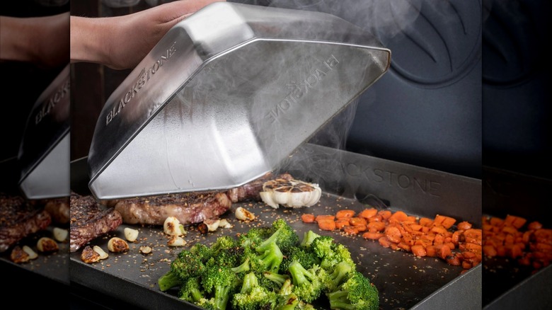 Hand lifting a Blackstone Medium Square Basting Cover off steamed broccoli