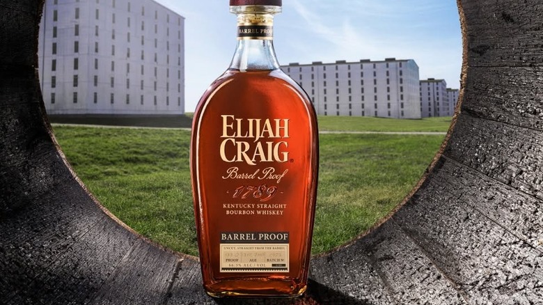 A bottle of Elijah Craig Barrel Proof shot inside of a barrel with warehouses shown in the background