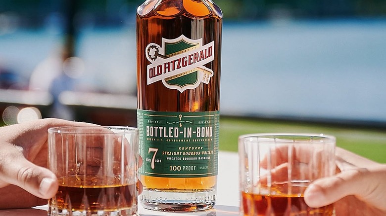 A bottle of Old Fitzgerald Bottled-in-Bond outside with people holding filled glasses either side