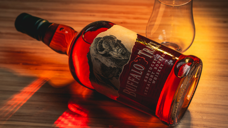 A bottle of Buffalo Trace laid down on a wooden surface next to an empty glass