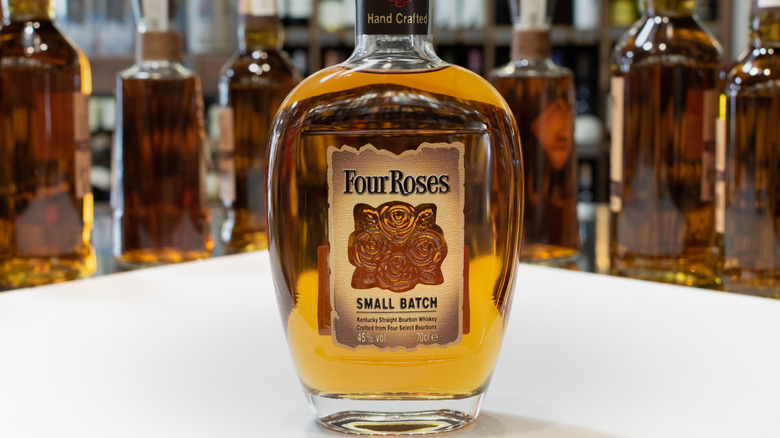 A bottle of Four Roses Small Batch posed on a white table with bottles shown in a blurred background