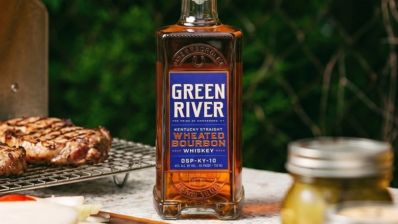 A bottle of Green River Wheated Bourbon place on a table outdoors in a BBQ setting