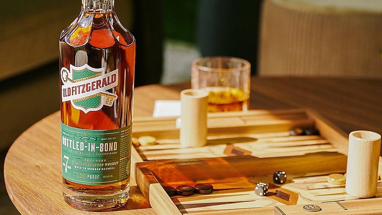 A bottle of Old Fitzgerald Bottled-in-Bond placed on a table next to a game and a filled glass