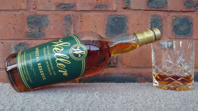 A bottle of Weller Special Reserve balanced on the rim of a filled glass in front of a brick background